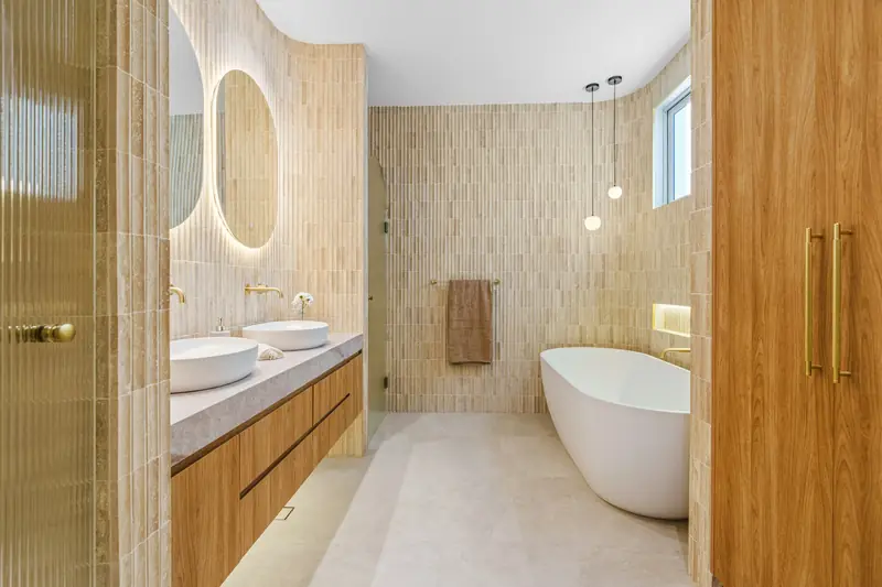 Bathroom with a freestanding bathtub, twin basins, stone tiles and timber joinery