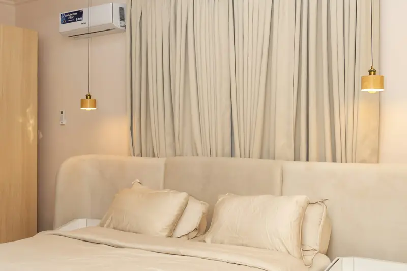 Bedroom with a cream upholstered bed, curtains and two brass pendant lights