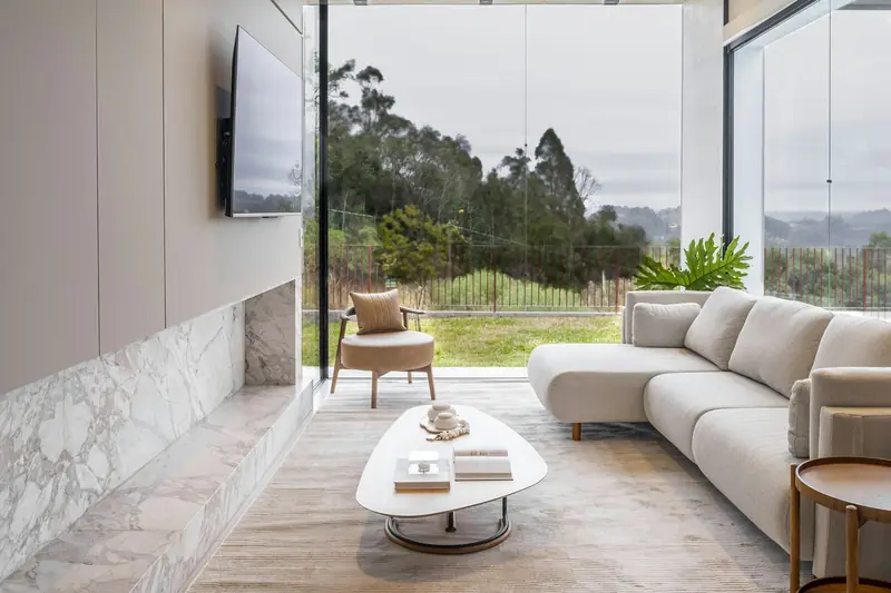 Living room with a marble-clad wall, a pale sectional sofa and floor-to-ceiling glass doors to a garden