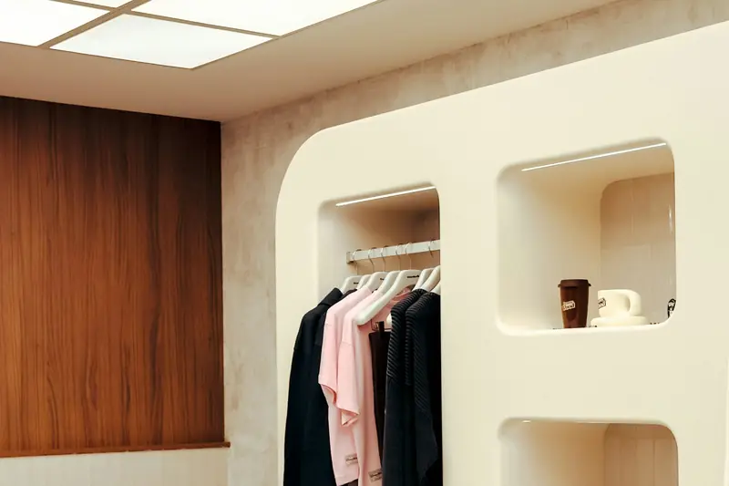 Retail wall display with a sculpted cream niche unit holding hanging clothes, lit by a ceiling light panel