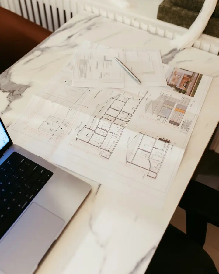 Architectural house plans and a laptop on a white marble desk